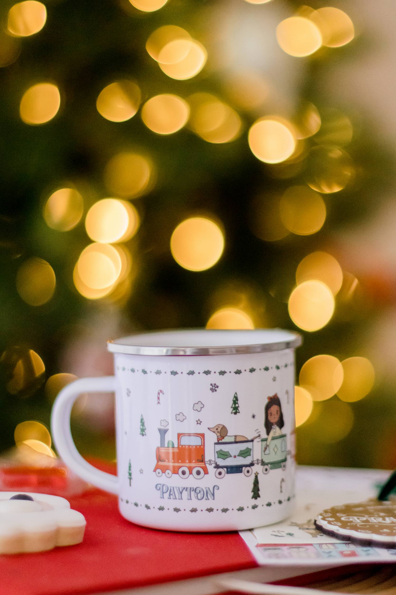Mug with train design on a table in front of a Christmas tree with lights.