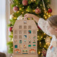 A festive wooden advent calendar depicting a multi-storied apartment building with Christmas decorations, being held by a child with a festive background.