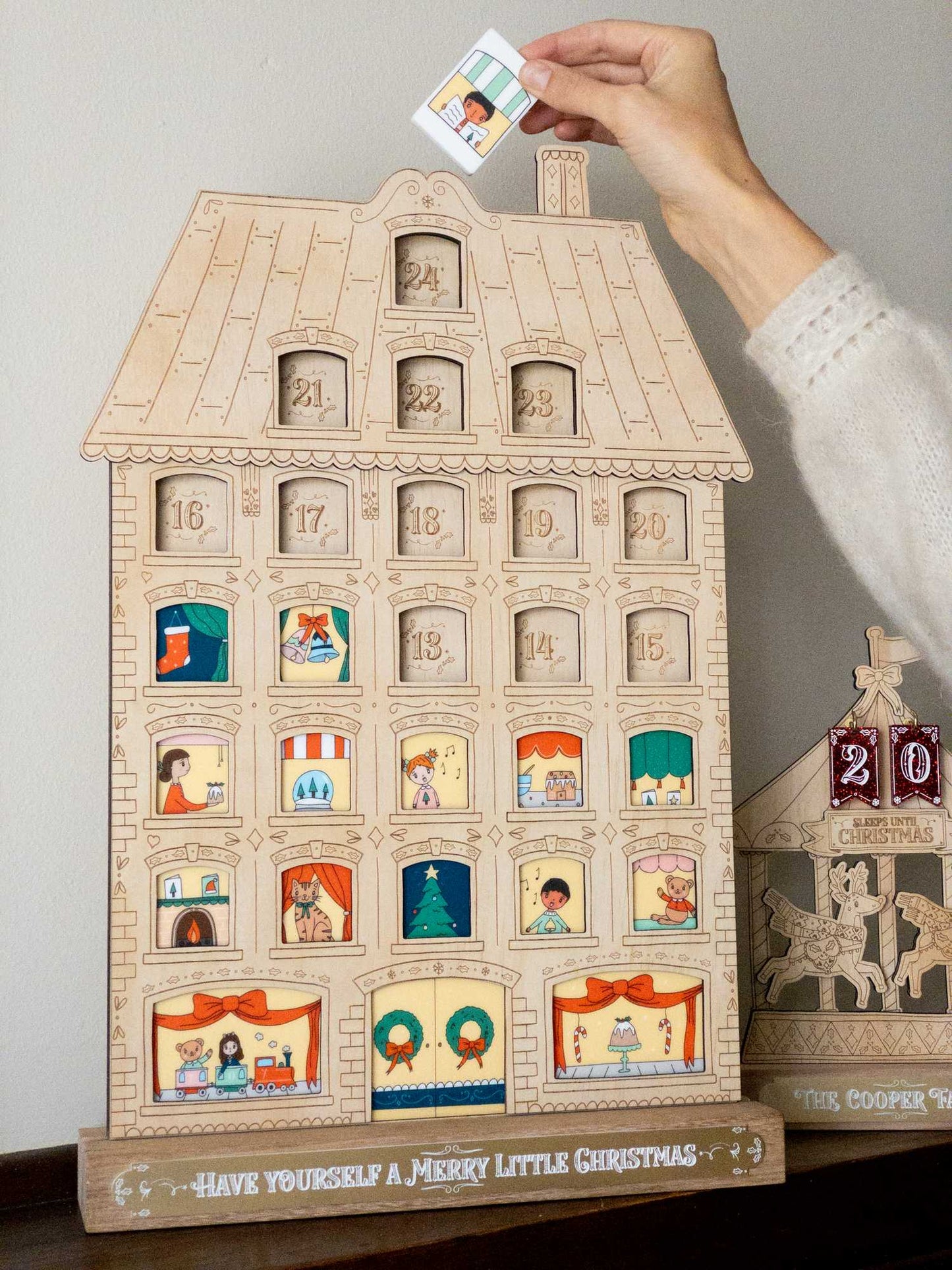 A festive advent calendar one a mantle with a tile about to be put it