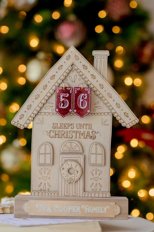 A wooden gingerbread house Christmas countdown with numbers 5 and 6 placed on it, with a festive background.