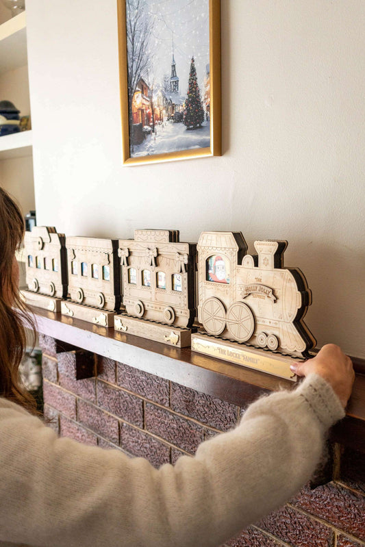 Wooden train advent calendar on a fireplace mantle with a person's arm reaching towards it.