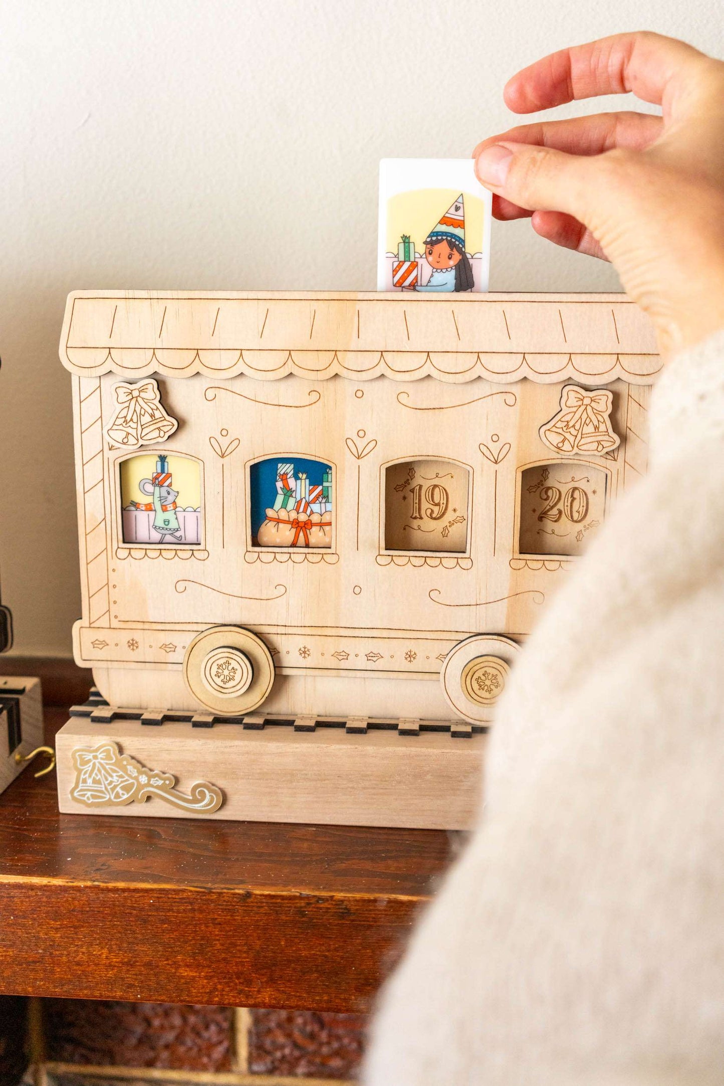 Wooden train advent calendar with small windows opening to reveal colorful figures, held by a hand.