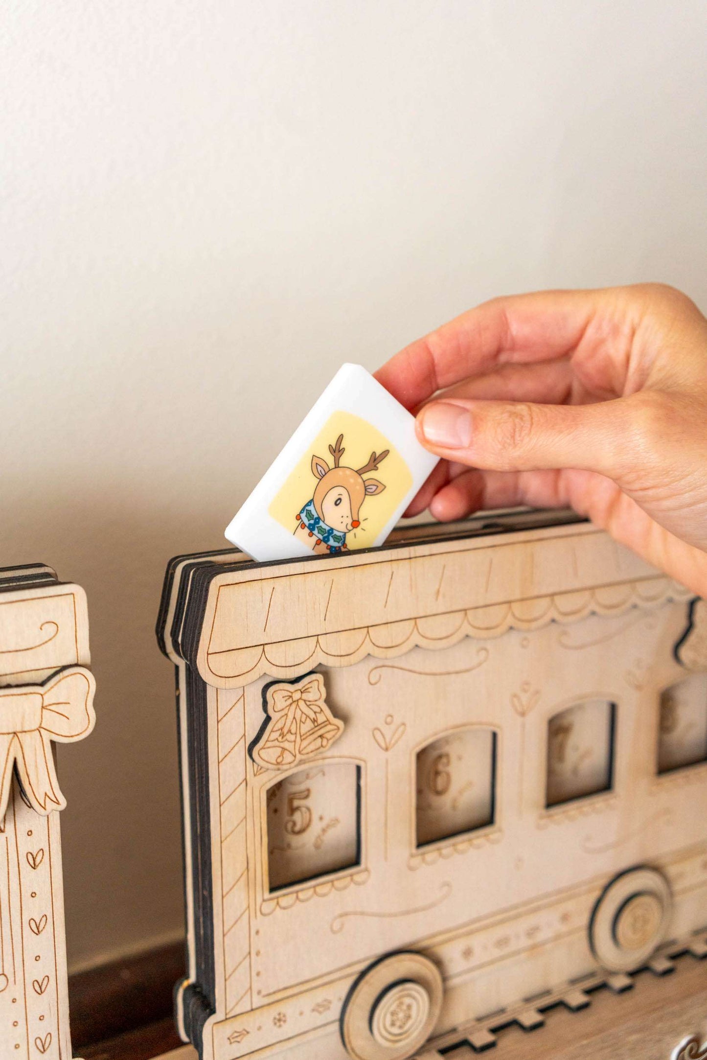 Hand placing a tile with a hand  illustrated character into a wooden advent calendar.