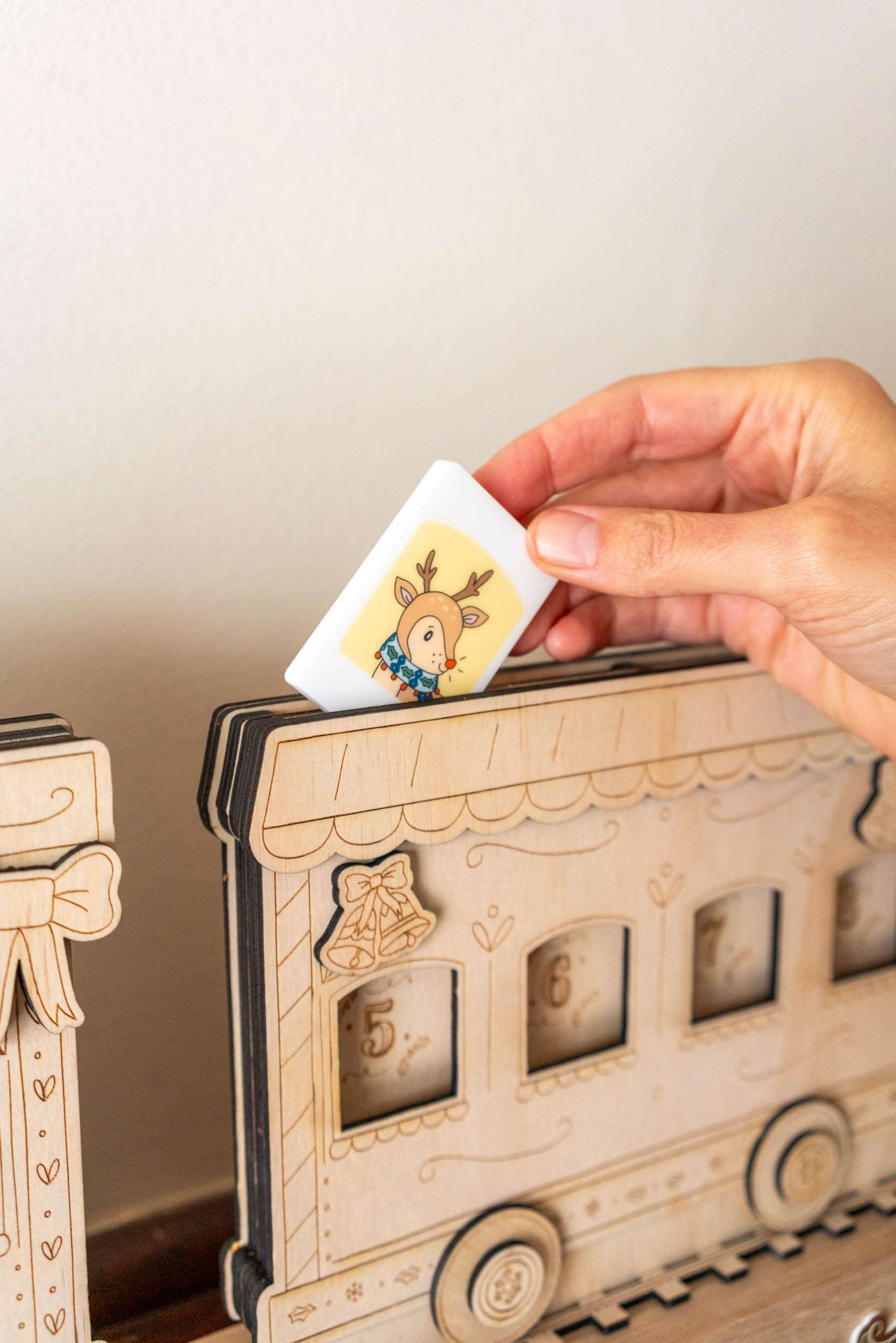 Hand placing a tile with a hand  illustrated character into a wooden advent calendar.