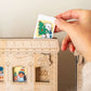 Wooden advent calendar with a hand placing a tile featuring a bear and Christmas tree.