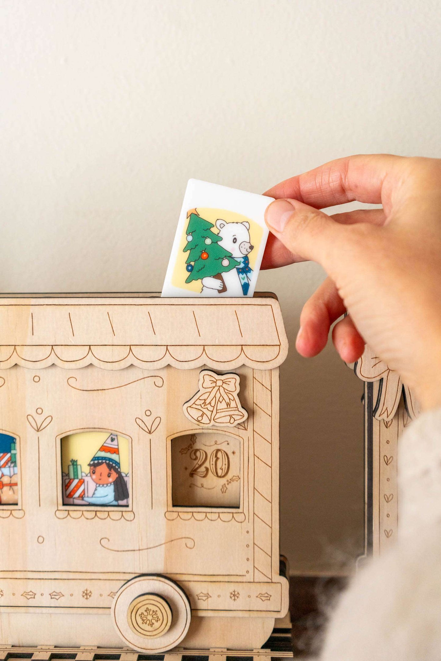 Wooden advent calendar with a hand placing a tile featuring a bear and Christmas tree.